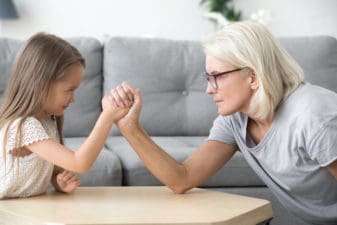 Old grandma and little granddaughter arm wrestling playing together