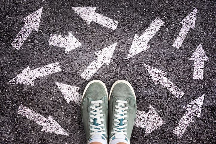 Sneaker shoes and arrows pointing in different directions on asphalt ground, choice concept