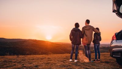 Family with small yellow dog embracing at hill and looking at sunset