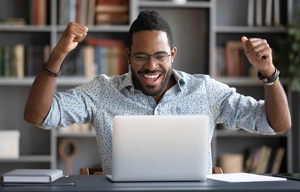 Happy african guy looking at laptop screen, cheering