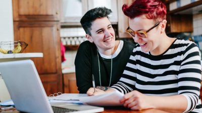 Female couple paying bills online at home, laughing