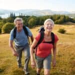 Portrait Of Senior Couple Climbing Hill On Hike Through Countryside In Lake District UK Together